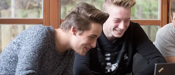 Drei Jugendliche der stationären Jugendhilfe schauen lachend in einen Laptop