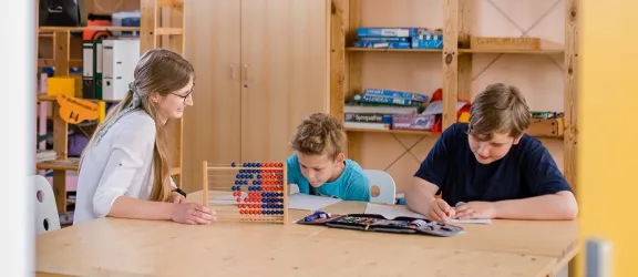 Zwei Kinder üben mit einer Lehrkraft am Tisch