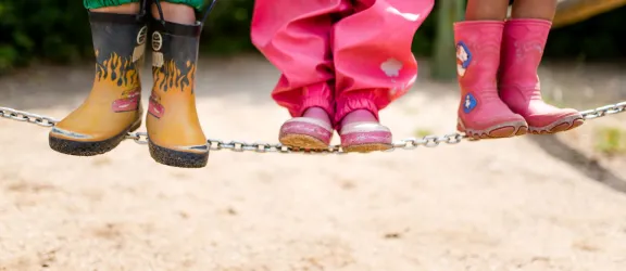 Kindergartenkinder stehen in Gummistiefeln nebeneinander auf Balancierseil