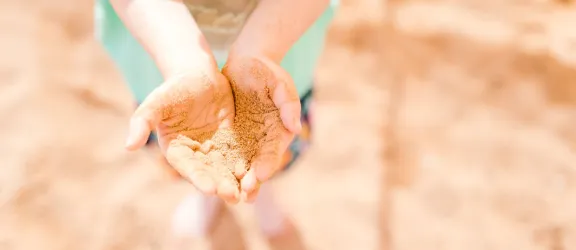 Kindergartenkind im Sandkasten hält Hände voller Sand vor sich