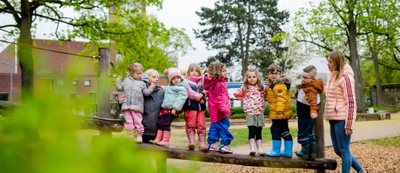Kinder stehen auf einem Balancierbaumstamm im Garten der Kita