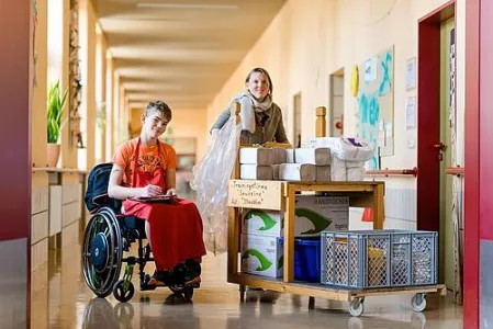 Ein junger Mensch im Rollstuhl mit einer Mitarbeiterin im Flur