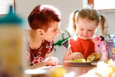 Erzieherin hilft Krippenkind beim Essen