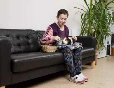 Frau sitzt am Sofa und streichelt einen Hamster
