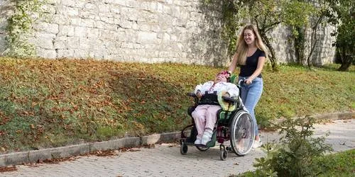 Mitarbeiterin schiebt eine Beschäftigte im Rollstuhl im Garten