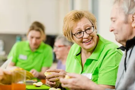 Mitarbeiter und Senioren schneiden gemeinsam Obst bei Tagespflege
