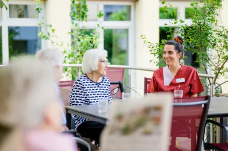 Pflegefachkraft und Bewohnerinnen des Seniorenheims im Gespräch im Garten