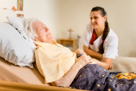 Im Bett liegende alte Frau mit Pflegerin