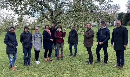 Neun Menschen stehen auf der Streuobstwiese vor einem Baum