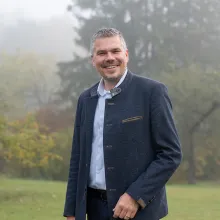 Diakon Alexander Loos steht vor Bäumen und lächelt in die Kamera