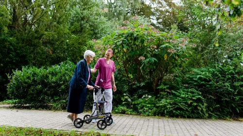 Eine ältere Dame und eine Pflegerin beim Spazieren