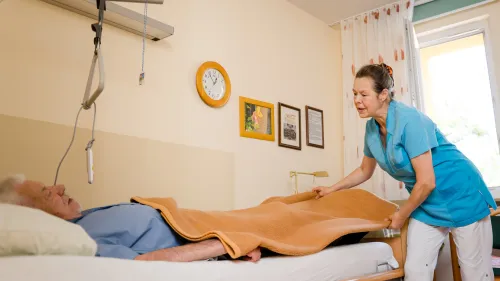 Eine Pflegefachkraft versorgt einen Klienten im Krankenbett
